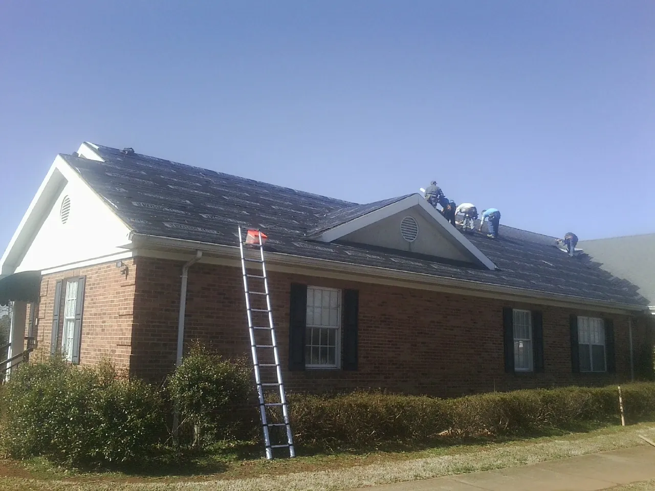 Crew tearing shingles off a brick ranch roof with a ladder set — Emergency Roof Repair work by our crew in Cecil