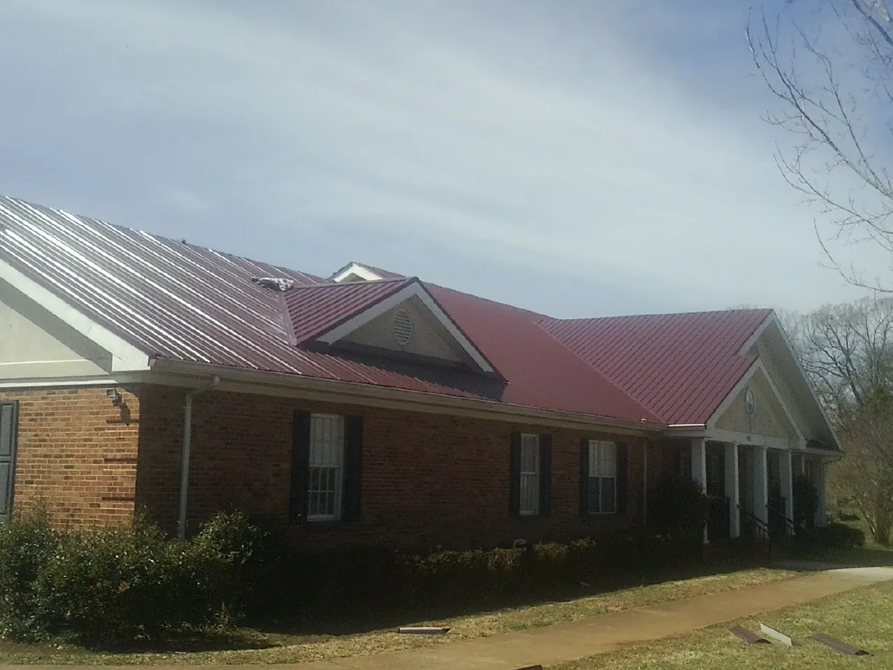 Red metal roof with gabled entries on a long brick building, from a Hail Damage Roof Repair job in Cecil
