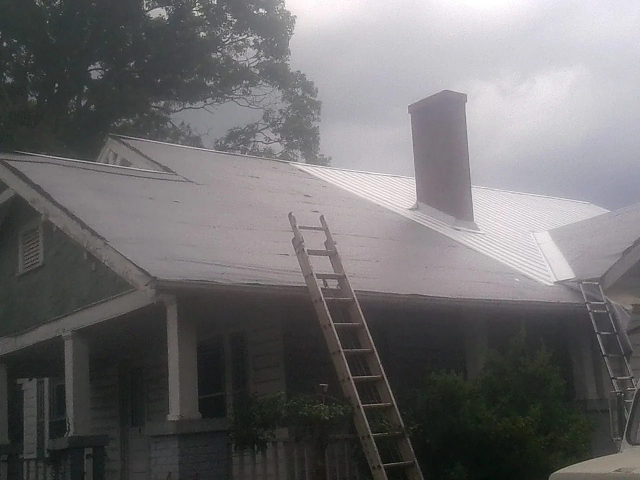 Ladders against a metal roof on an older home with a brick chimney in Cecil