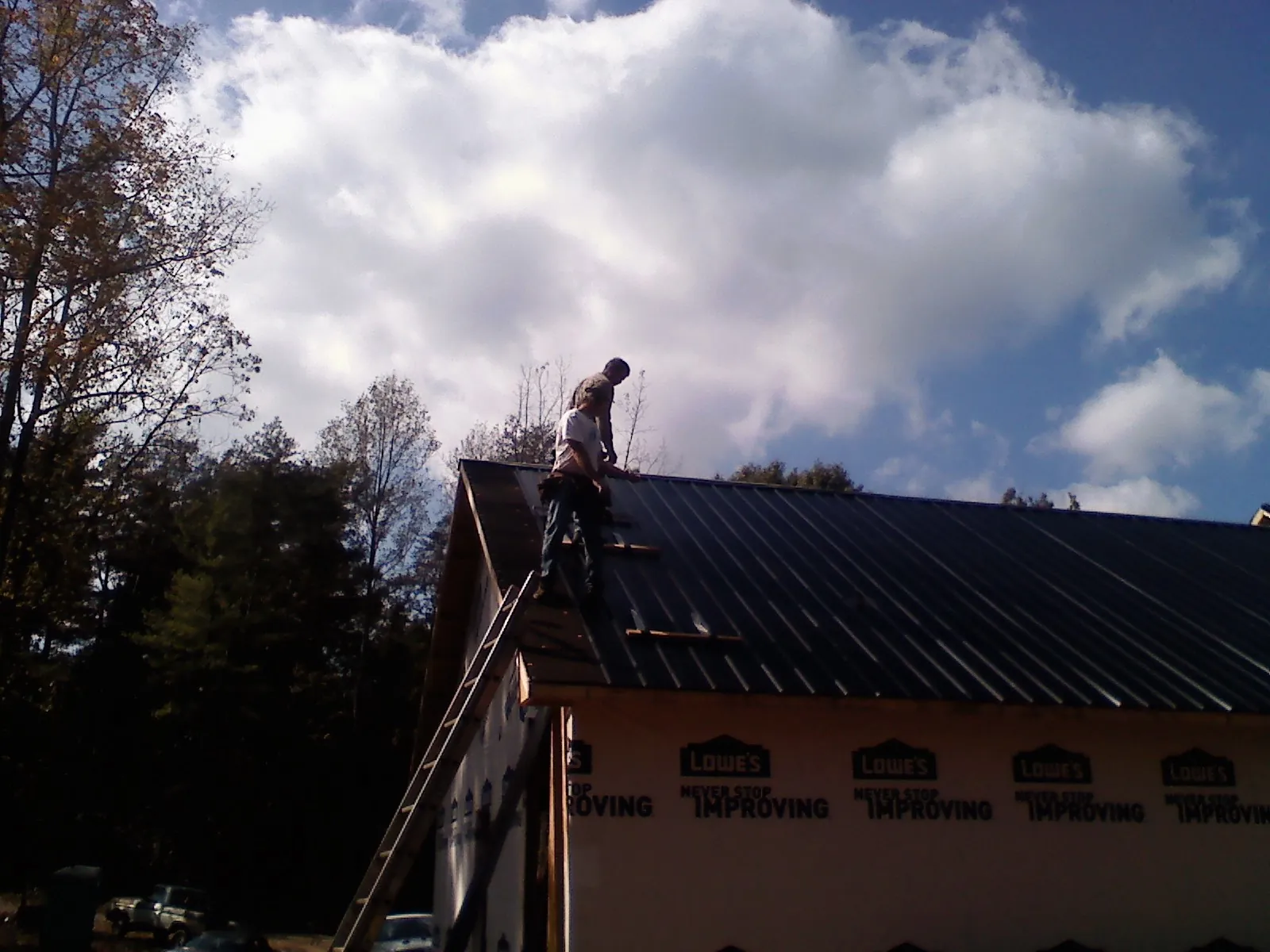 Roofer fastening dark metal panels high against a cloudy sky, from a Roof Inspection job in Cecil