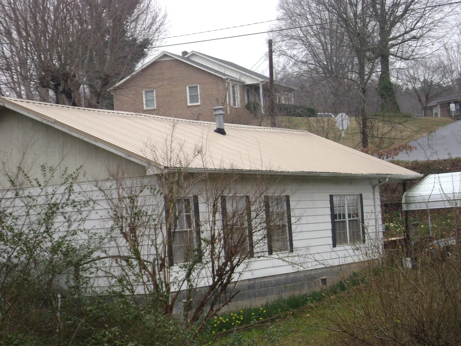 Tan metal roof on a white sided house set into a hillside — Commercial Roofing by Roofing Brothers in Cecil